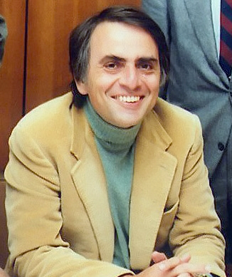 Carl Sagan, from image of the Planetary Society, cropped to size. He is smiling and looking at the camera, wereaing a beige jacket and green turtle neck