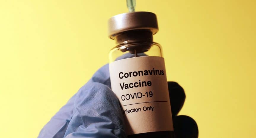 Covid Vaccine bottle with a syringe inserted into it being held by a hand in surgical glove by Hakan Nural Unsplash - 360onhistory.com
