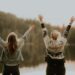 Two women with raised hands by a lake. Photo by Priscilla Du Preez on Unsplash