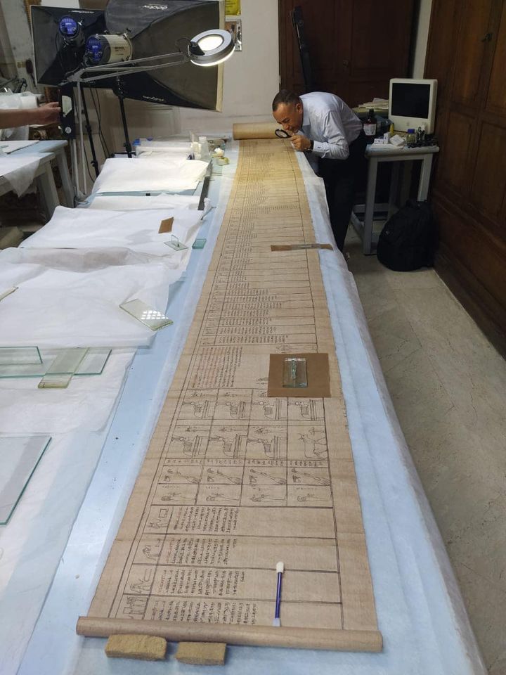 The 52-foot-long scroll was found at Saqqara in May 2022. It contains chapters from the Book of the Dead. It was recently restored and translated into Arabic and is now on display at The Egyptian Museum in Cairo. The text is written in hieratic, a script derived from hieroglyphs. Here it is placed on a long table with a man looking at it.