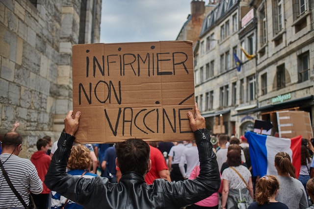 A focus on a man within a protesting crowd holding up a sign saying infirmier non vaccine. By Jordan Bracco on Unsplash