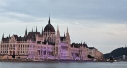 Hungarian Parliament at sunset with the Chain Bridge to the right of the image. The building is in a purple glow due to lights.