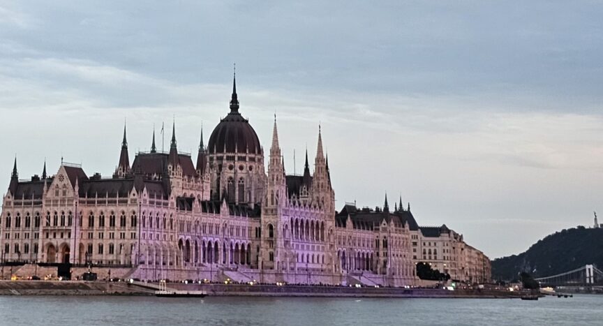 Hungarian Parliament at sunset with the Chain Bridge to the right of the image. The building is in a purple glow due to lights.
