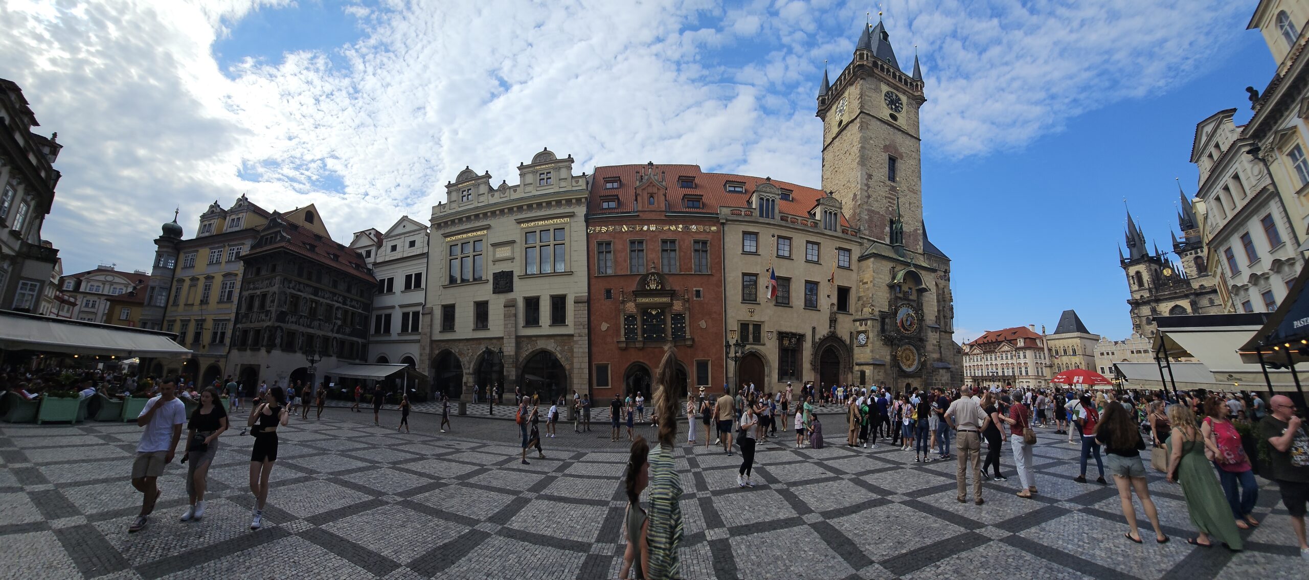Old Town Square (Staroměstské náměstí) showing the Prague Astronomical Clock and peopel walking around. Blue sky with some wispy clouds in the sky. Image by 360onhistory.com