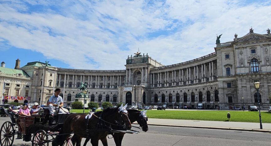 Front view of Hofburg Palace with a horse buggy passing in front of it.