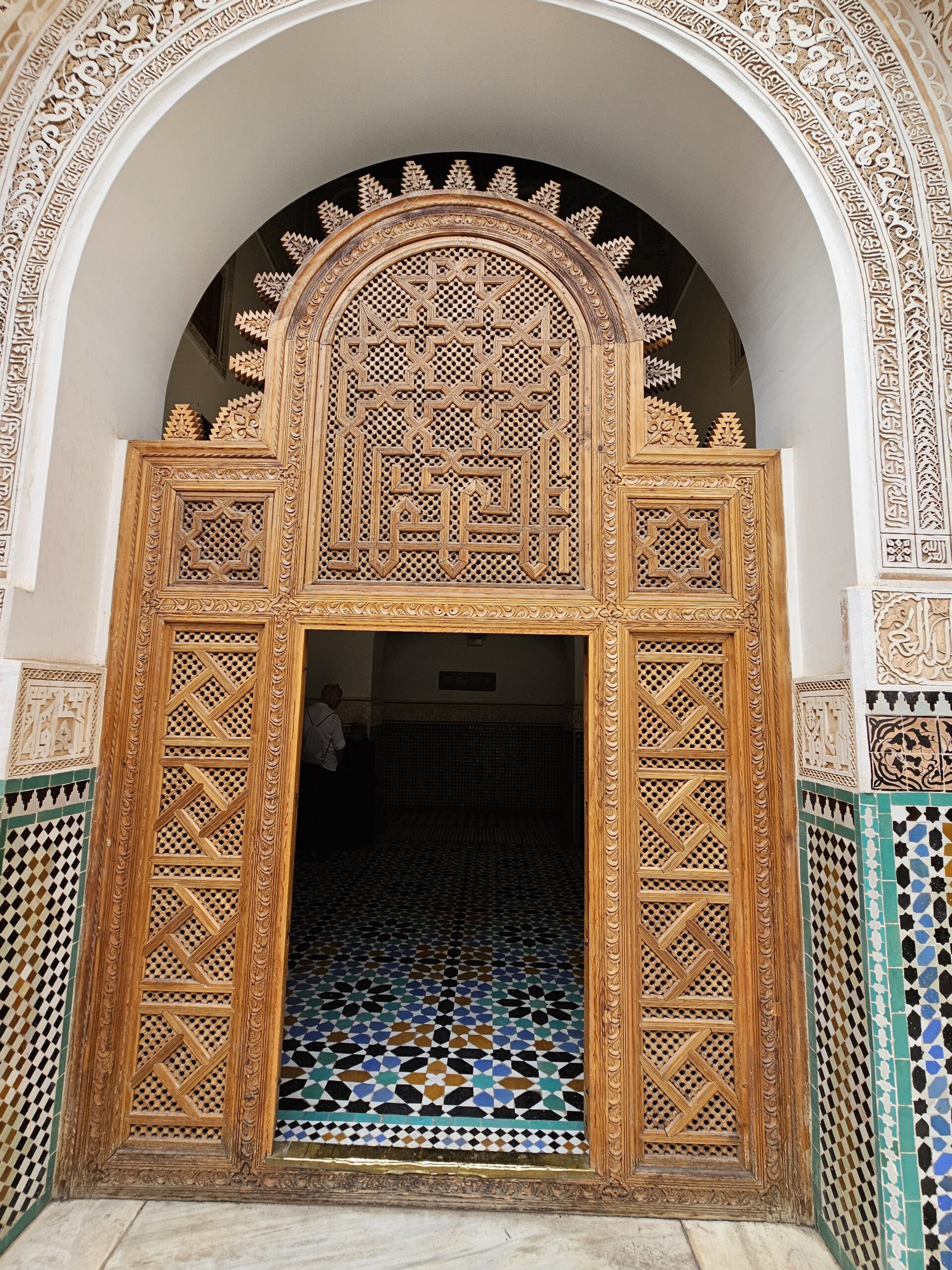 A carved wooded door and alcove with carvings at the top section and coloured mosaic at the lower third. Image by 360onhistory.com