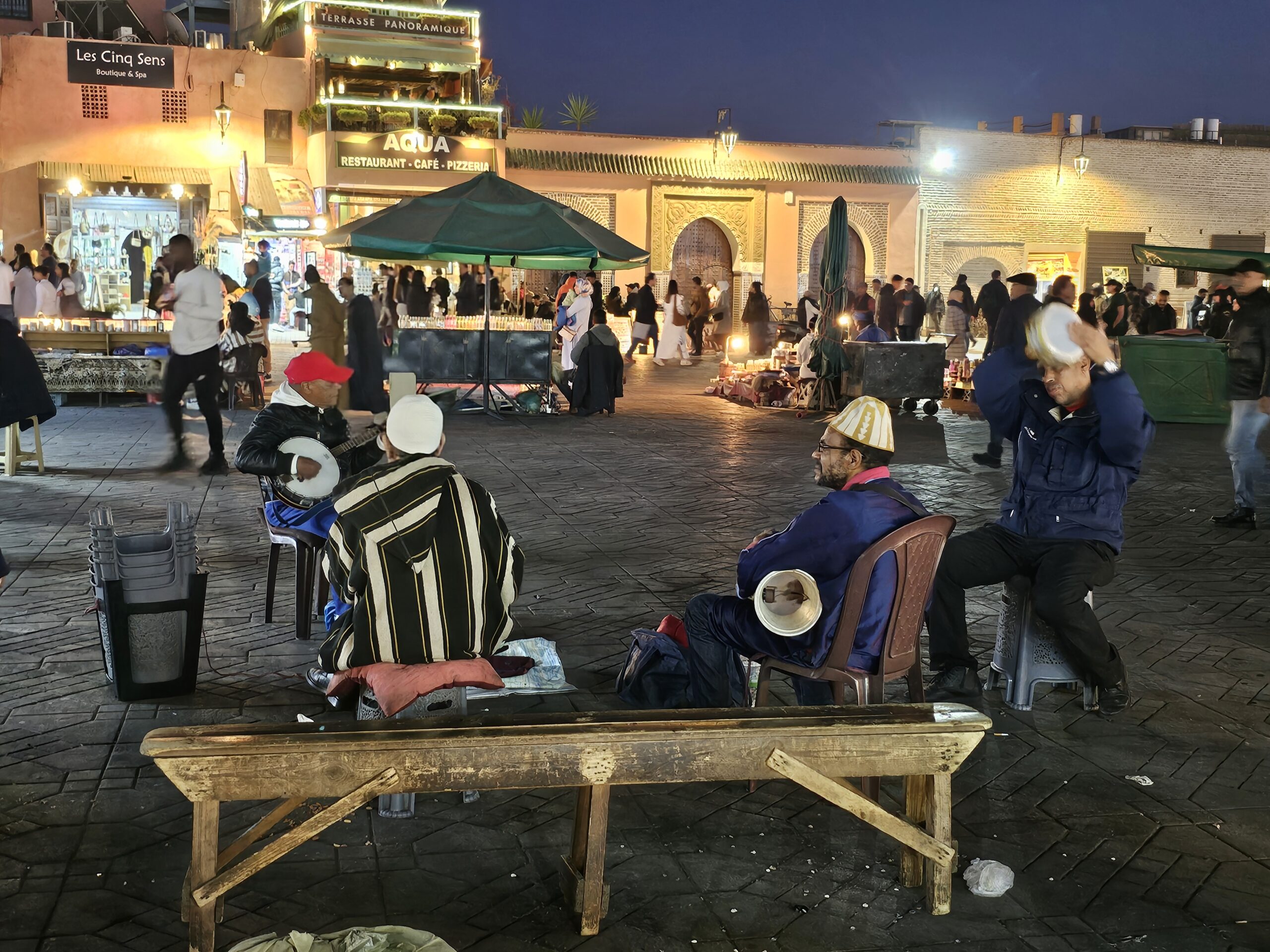 Two men sitting on plastic chairs with their back to the camera looking at the activity around Jemaa el Fnaa, Marrakesh. Image by 360onhistory.com