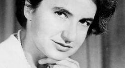 Black and white photo of Rosalind Franklin. She is wearing a pearl necklage and looking sideways at the camera with a slight smile. Her chin is on the fingers of her hand.