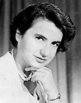 Black and white photo of Rosalind Franklin. She is wearing a pearl necklage and looking sideways at the camera with a slight smile. Her chin is on the fingers of her hand.